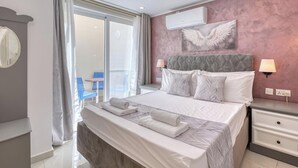 A hotel room with a bed, bedside lamps, a wall-mounted air conditioner, a window with curtains, and a view of the outside.