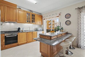 A kitchen with wooden cabinets, a granite countertop, a built-in oven, a microwave, and a sink. - Cozy 'Casa Refugio' Apartment with Balcony, Wi-Fi and Air Conditioning (Armação de Pêra)