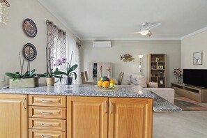 A kitchen with a granite countertop, wooden cabinets, a ceiling fan, and a dining area with a table and chairs. - Cozy 'Casa Refugio' Apartment with Balcony, Wi-Fi and Air Conditioning (Armação de Pêra)