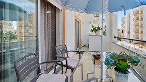 A balcony with a glass table, two chairs, a potted plant, and a blue umbrella.