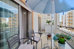 A balcony with a glass table, two chairs, a potted plant, and a blue umbrella. - Cozy 'Casa Refugio' Apartment with Balcony, Wi-Fi and Air Conditioning (Armação de Pêra)