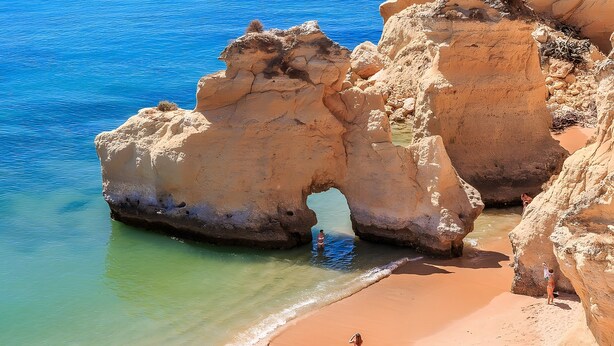 A beach with a natural rock formation and clear blue water.