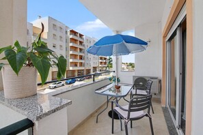 Een balkon met een tafel, stoelen, een bloempot en een blauwe parasol.