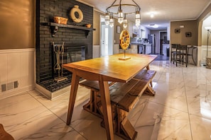 A dining area with a wooden table, bench seating, a fireplace, and a kitchen in the background. - Moss drive retreat - Close to the woods (Douglasville)