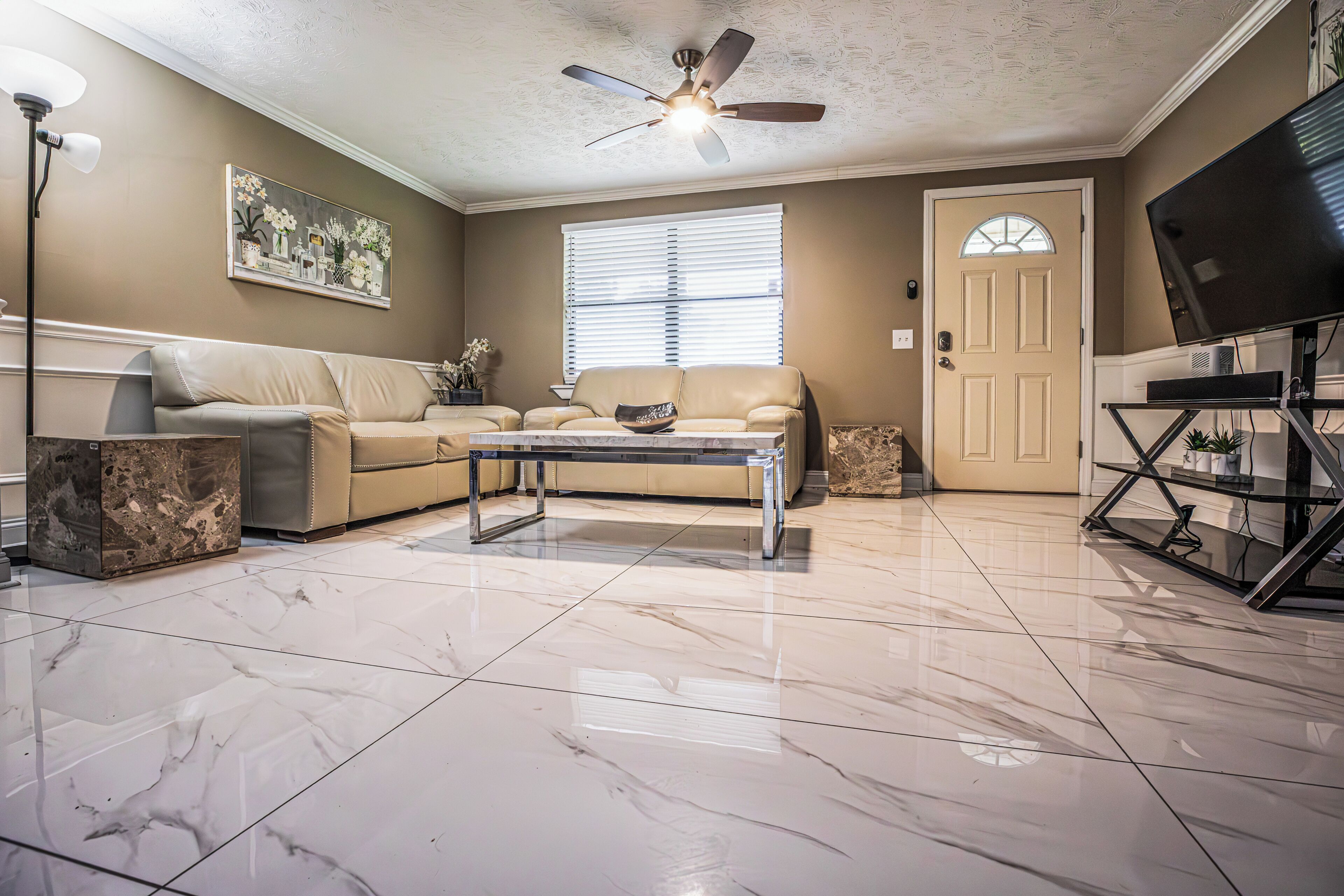 A living room with a ceiling fan, a sofa, a coffee table, a TV on a stand, and a door with a window.