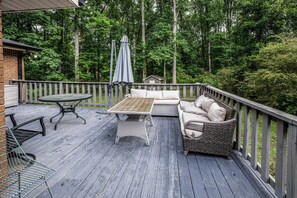 A wooden deck with outdoor furniture, including a table and a sofa, surrounded by a wooden railing. - Moss drive retreat - Close to the woods (Douglasville)