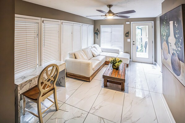 A living room with a white sofa, a wooden chair, a coffee table, and a ceiling fan. - Moss drive retreat - Close to the woods (Douglasville)