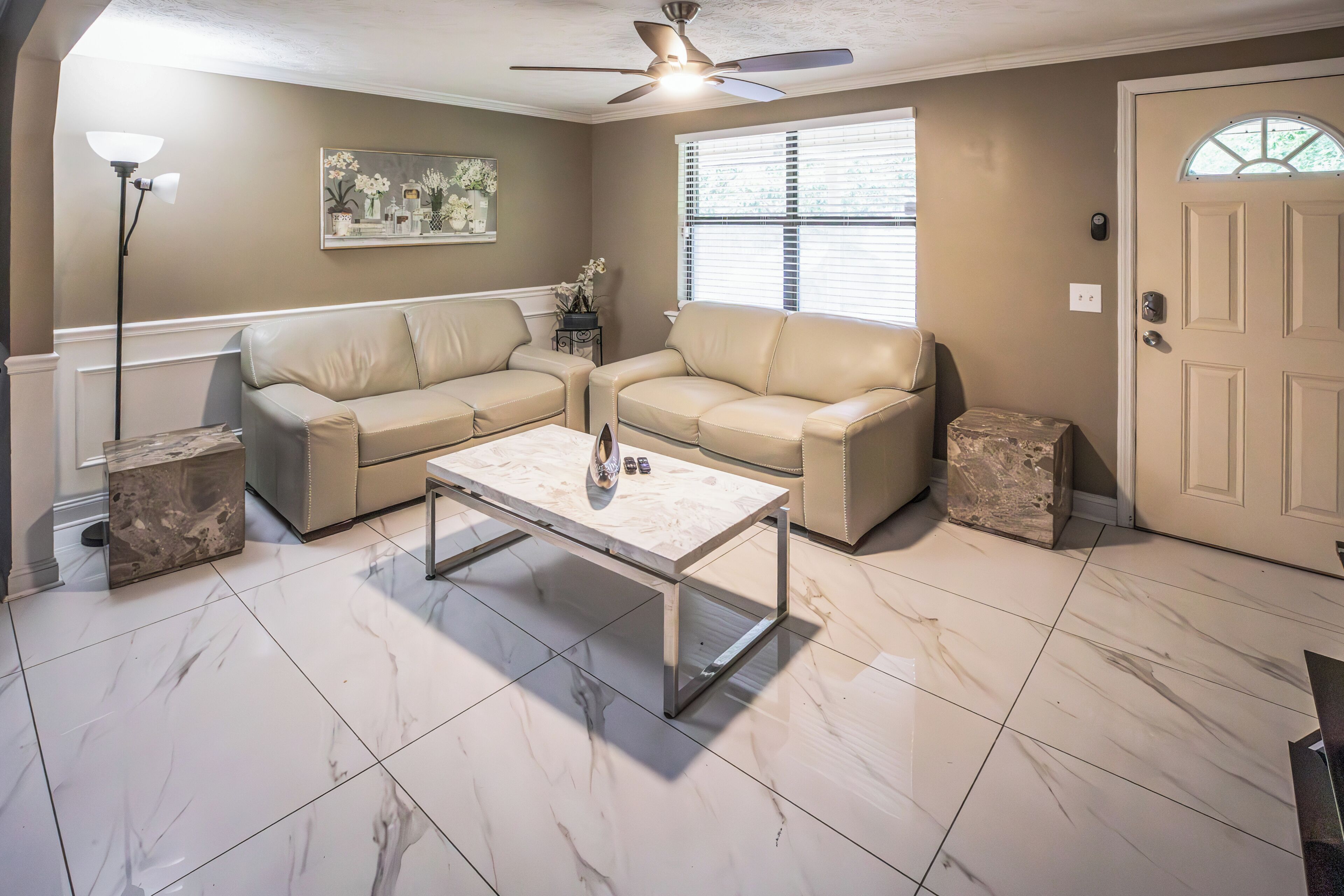 A living room with a beige sofa set, a marble coffee table, a floor lamp, and a ceiling fan.