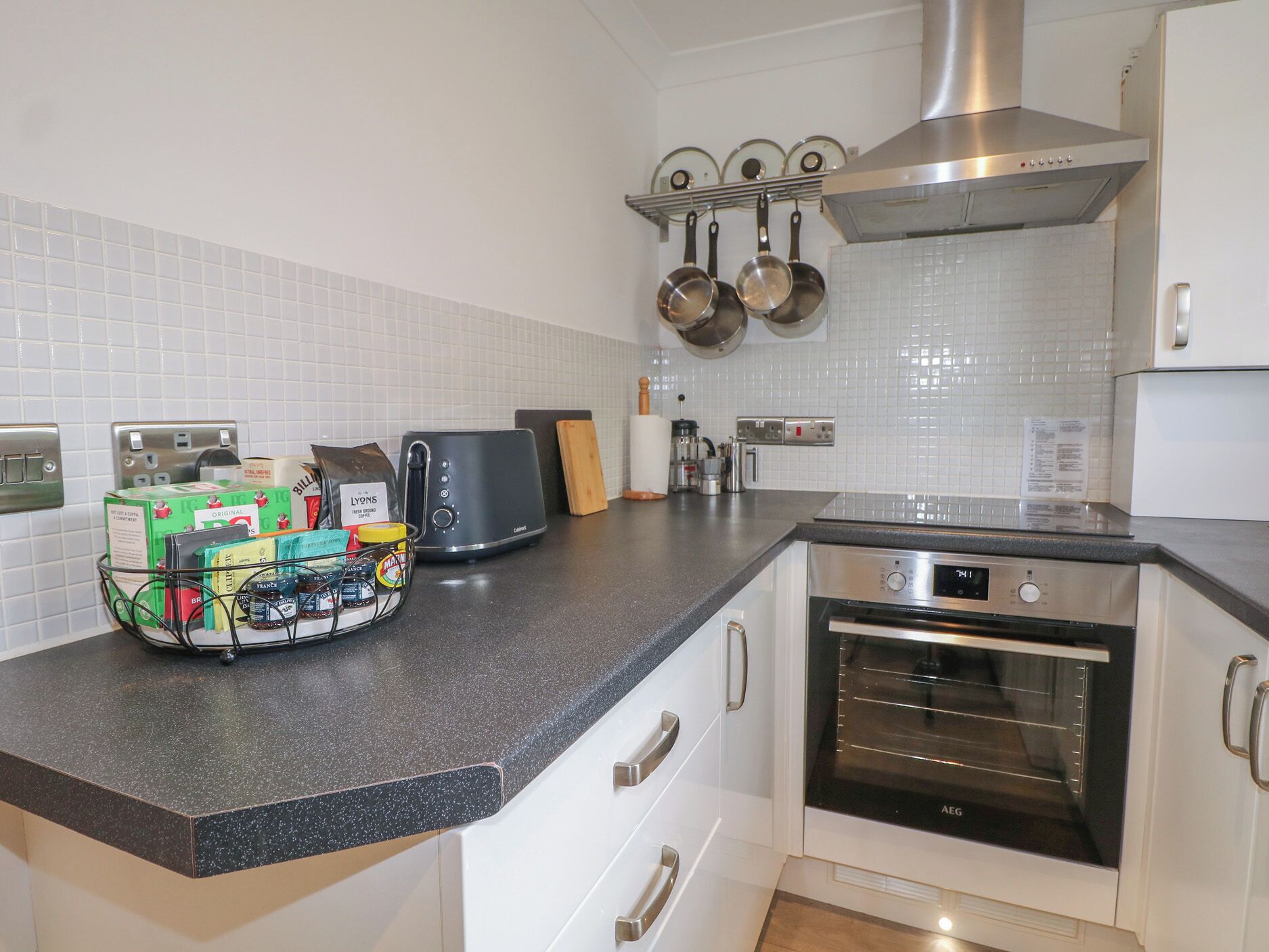 A kitchen with a countertop, a toaster, a kettle, a stove, and a hanging pot rack.