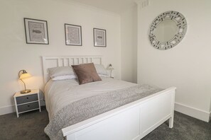 A bedroom with a bed, a nightstand, a lamp, and three framed pictures on the wall. - Foreshore (Deal)