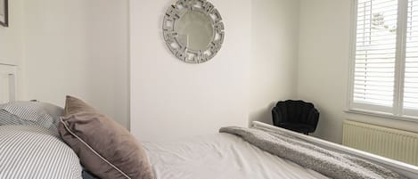 A bedroom with a bed, a round mirror, a chair, and a window with blinds.