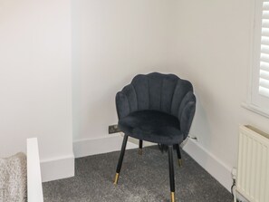 A corner room with a dark-colored chair, white walls, a radiator, and a carpeted floor. - Foreshore (Deal)