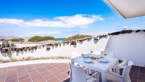 Une terrasse avec une table dressée pour deux personnes, offrant une vue sur la plage et l’océan.