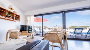Un salon moderne doté d’une grande fenêtre, de meubles en osier, d’un téléviseur à écran plat et offrant une vue sur la plage.