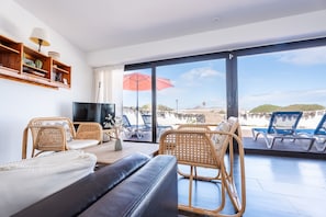 A modern living room with a large window, wicker furniture, a flat-screen TV, and a view of the beach. - Quicksand • Ocean views • Beach 1 min • LVH (Famara)