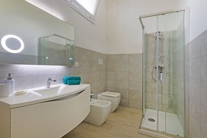 Une salle de bain moderne avec une douche à parois de verre, un grand miroir et un meuble-lavabo blanc.
