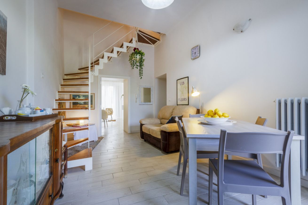 Un espace repas comprenant une table, des chaises, un canapé et un escalier menant à une autre pièce.
