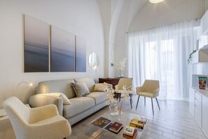 Ein modernes Wohnzimmer mit einer Couch, Sesseln, einem Couchtisch mit Büchern, einem Spiegel und Kunstwerken an der Wand.