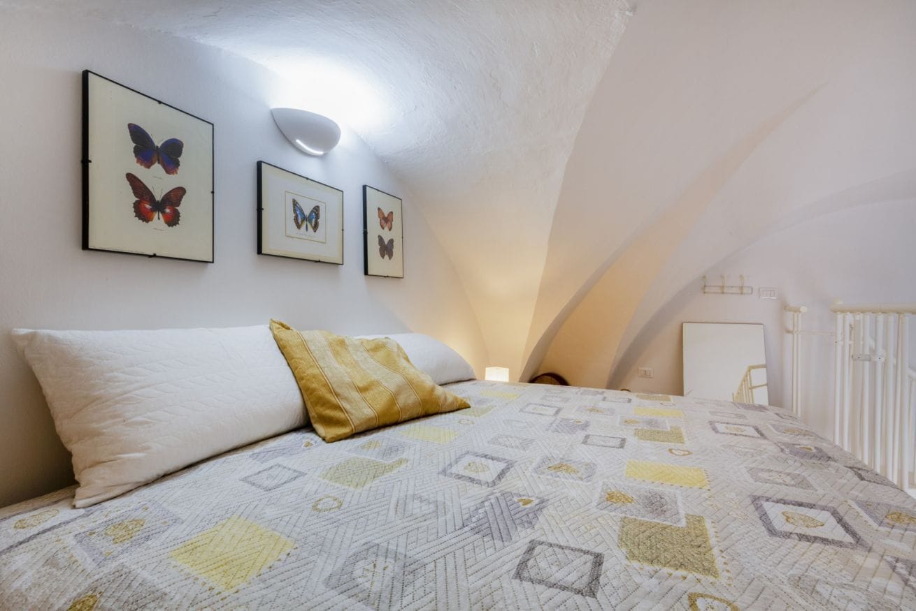 Une chambre à coucher avec un lit, des oreillers, une lampe fixée au mur et des œuvres d’art représentant des papillons, encadrées.