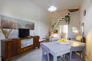 A modern living room with a wooden cabinet, a flat-screen TV, a dining table with chairs, and a staircase leading to an upper level. - Spacious two-level apartment, ideal for four people, with two bedrooms, two bathrooms, private parking, and a pleasant furnished internatl garden for relaxing outdoors. Located in the center of Campi Salentina, in a quiet residential area, it's just a 15 (Campi Salentina)