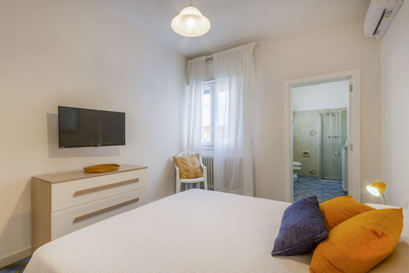 Habitación de hotel con cama, televisión, silla, escritorio y baño visible a través de una puerta abierta.