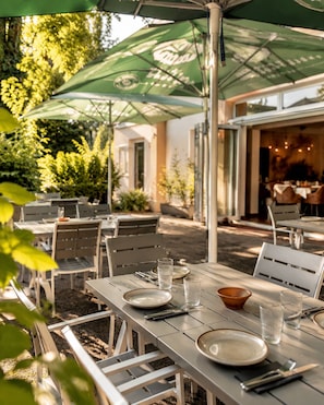 An outdoor dining area with tables and chairs, umbrellas, and a view of the restaurant interior.