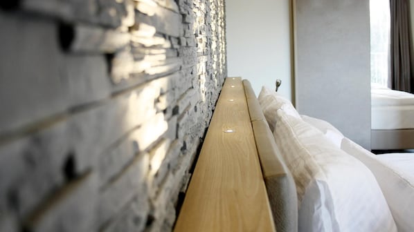 A bed with a wooden headboard against a textured wall, a window with curtains, and a bedside table. - Waidplatz Hotel (Teningen)