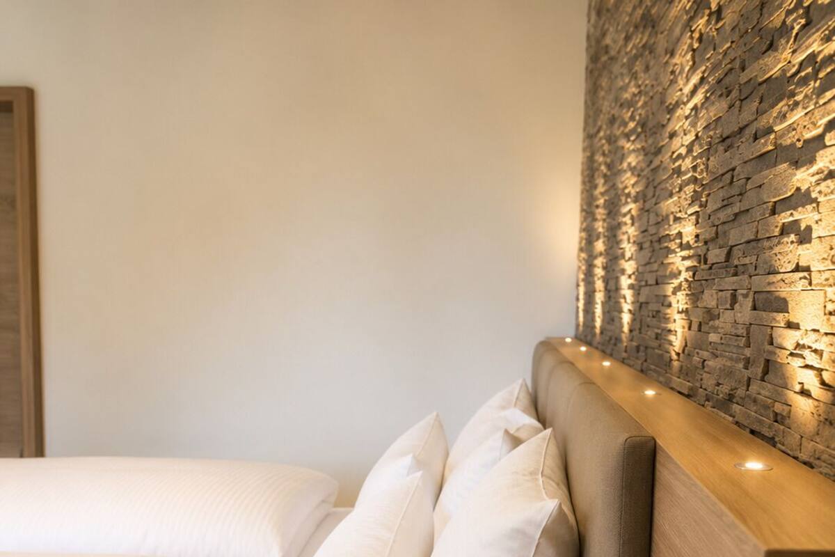 A bed with white linens, a headboard with a built-in lamp, and a wooden bedside table.