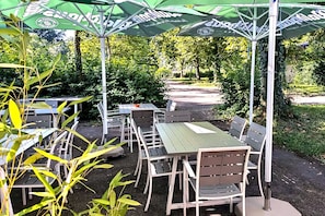 An outdoor patio area with tables and chairs under umbrellas, surrounded by greenery. - Waidplatz Hotel (Teningen)