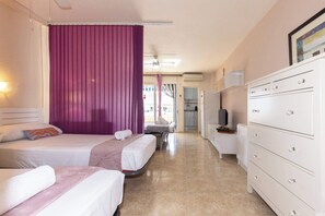 Ett hotellrum med två sängar, ett stort fönster med lila gardiner, en vit byrå och en tv.