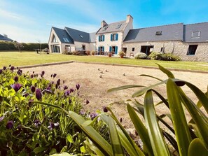 A large house with a paved courtyard, surrounded by greenery and flowers.