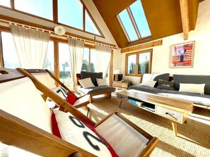 A room with a loft bed, a sofa, a coffee table, and a view of the outdoors.