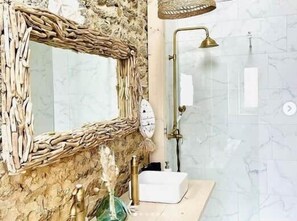 A bathroom with a rustic mirror, a handheld showerhead, and a marble wall.
