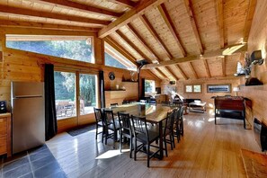 Interno di una baita in legno con zona pranzo, angolo cottura e ampie finestre.