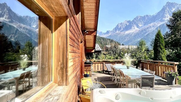 Une cabane en bois dotée d’un bain à remous et d’un espace extérieur aménagé, offrant une vue sur un paysage montagneux.