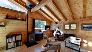 L’intérieur d’un chalet en bois, avec une cheminée, des étagères à livres, un fauteuil à bascule et une table à manger.