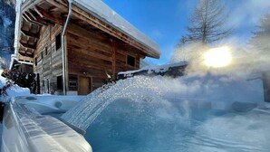 Una cabaña de madera con un jacuzzi, rodeada de nieve.