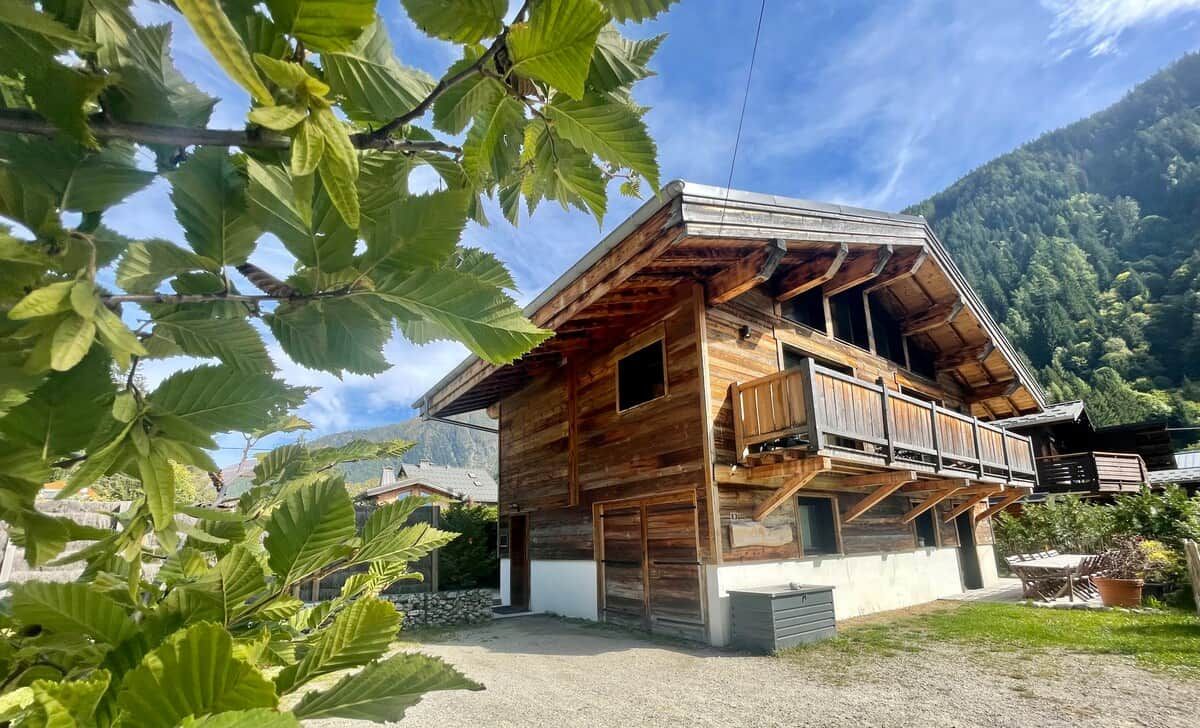 Una cabaña de madera con balcón, rodeada de vegetación y montañas.