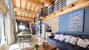 Amplia sala de estar con techo de madera, un sofá oscuro, una mesa de comedor y una cocina al fondo.