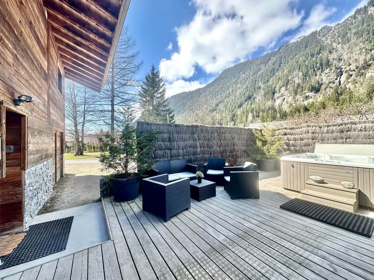 Une terrasse en bois avec des meubles d’extérieur, un jacuzzi et une vue sur les montagnes.
