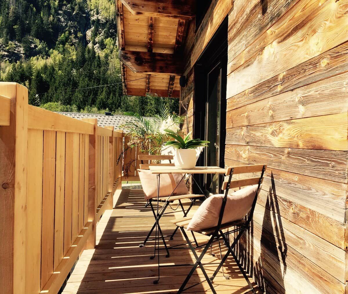 Una terraza de madera con una mesa y sillas, rodeada por un cerco de madera y una planta en maceta.