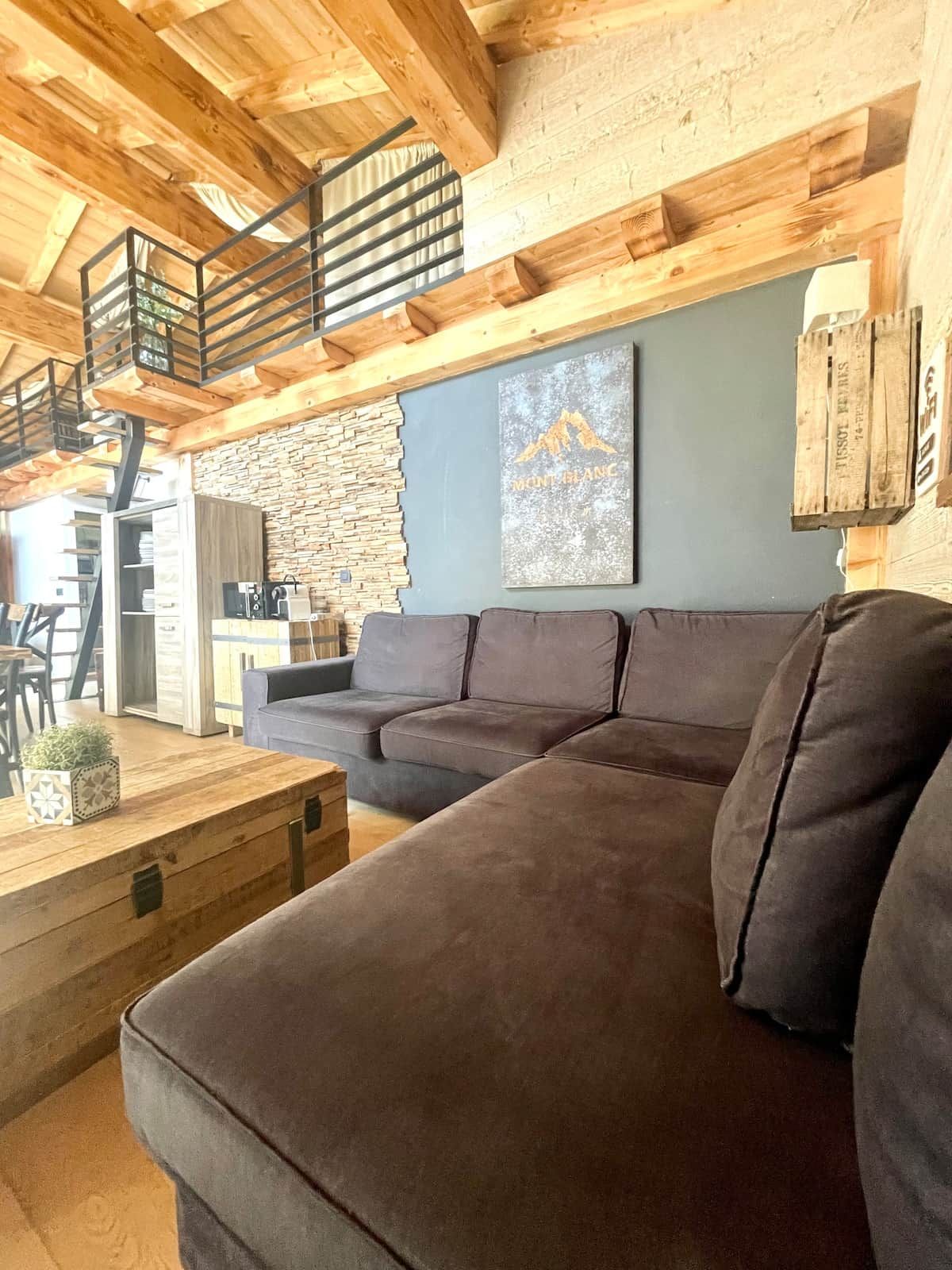 Una sala de estar acogedora con un sofá modular, una mesa de centro de madera y una pared de piedra.