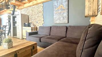 Una sala de estar acogedora con un sofá modular, una mesa de centro de madera y una pared de piedra.