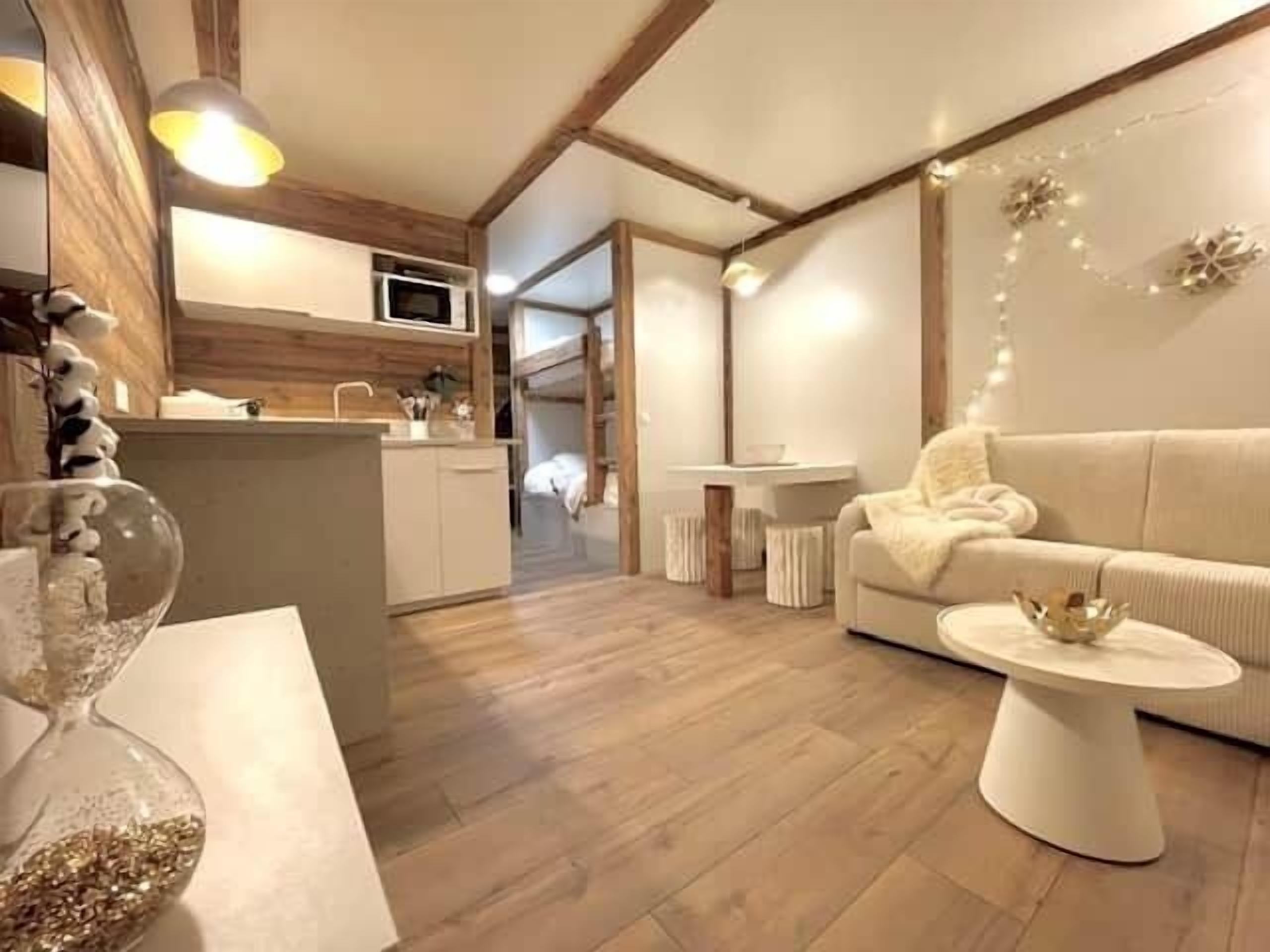 Un interno moderno con pavimento in legno, un divano bianco, un piccolo tavolino e un angolo cottura con forno a microonde.