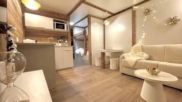Un interno moderno con pavimento in legno, un divano bianco, un piccolo tavolino e un angolo cottura con forno a microonde.