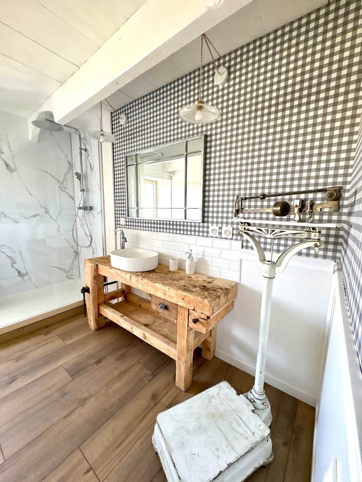 Un bagno con una parete a scacchi, un mobile lavabo in legno, una doccia in marmo e un lavandino bianco.