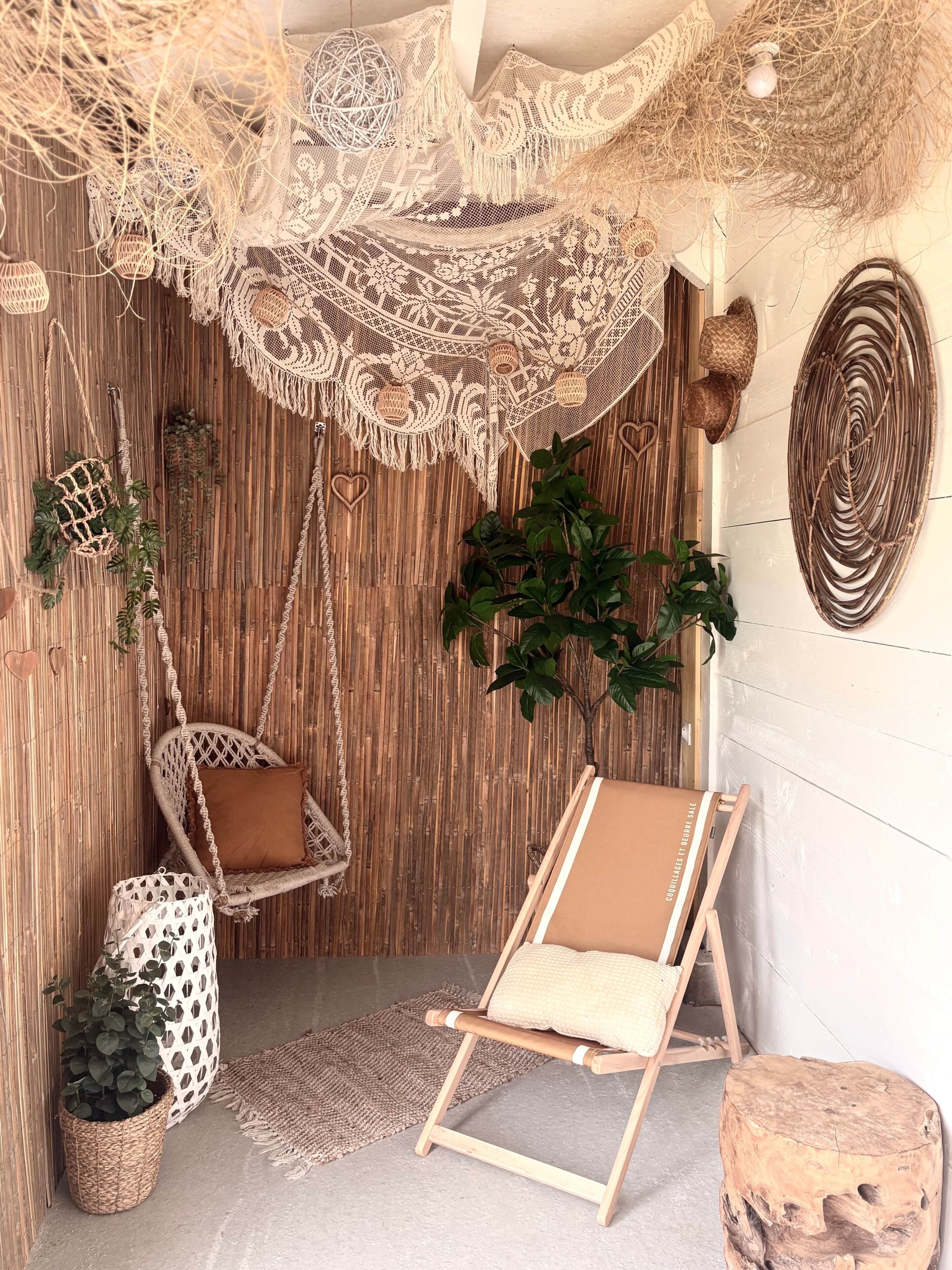 Ein Zimmer mit Hängestuhl, einem Holzschemel, einem kleinen Tisch und einer Wand mit gewebten Dekorationen.