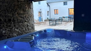 Uma banheira de hidromassagem com jatos, uma parede de pedra e vista para um edifício com área externa para sentar.