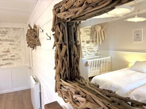 A rustic room with a large wooden mirror, a white crib, and a stone wall.