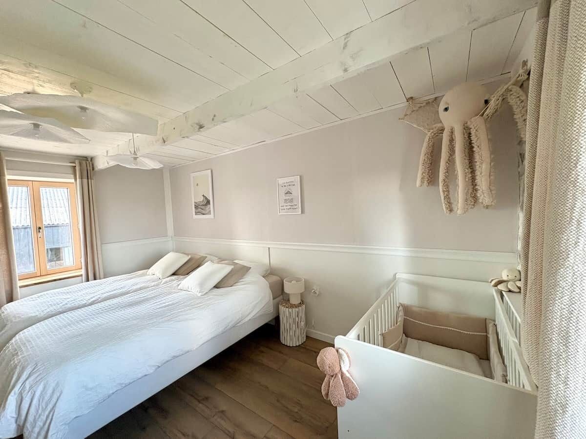 A bedroom with a double bed, a crib, a window with curtains, and a ceiling fan.